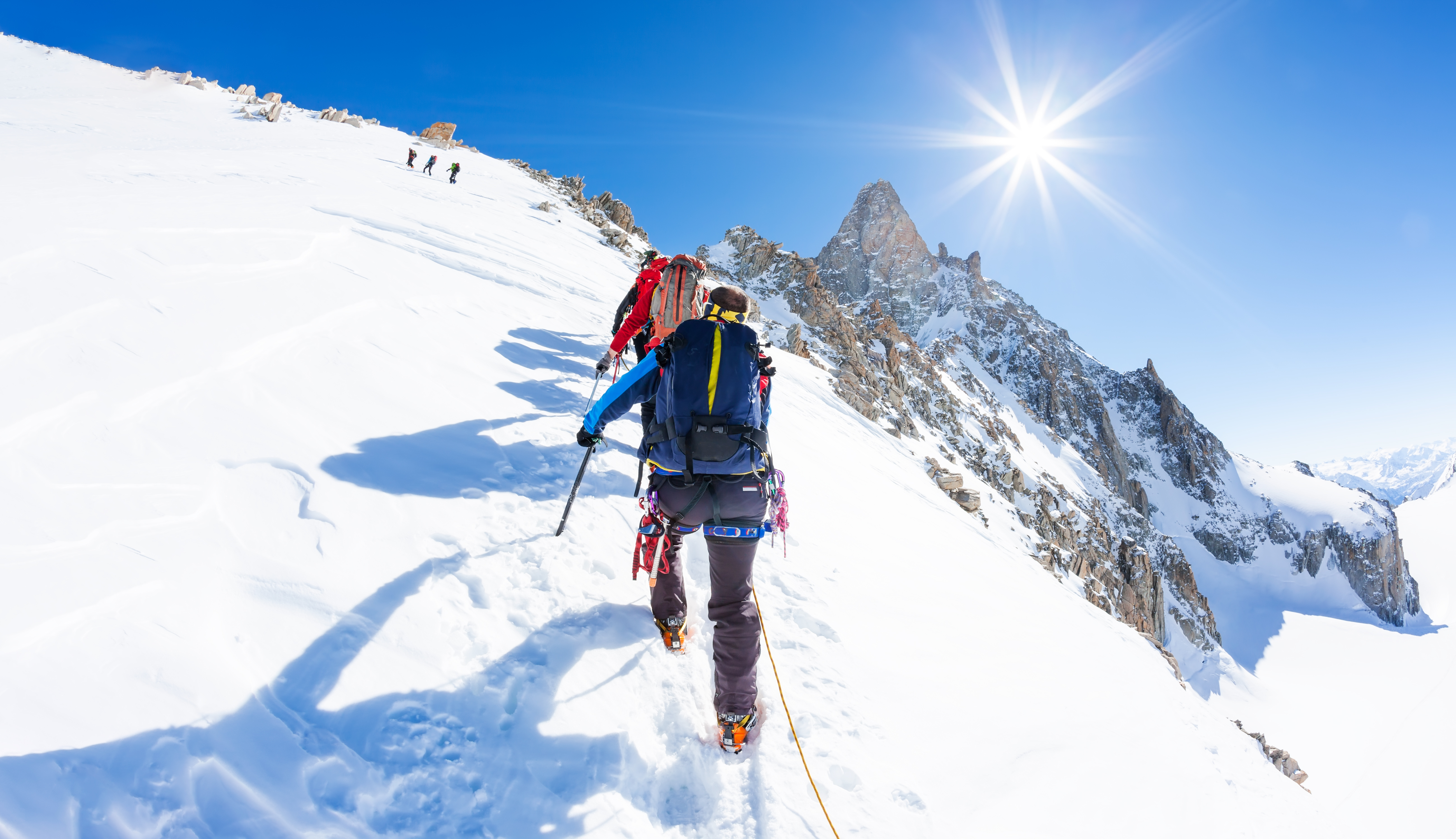 Mountaineers climb a snowy peak. In background the famous peak Dent du Geant in the Mont Blanc Massif, the highest european mountain. The Alps, Chamonix, France, Europe.